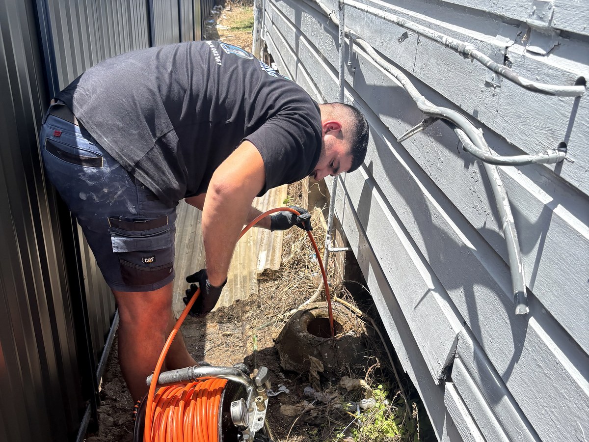 GPS plumber feeding a high-pressure jetting hose into an outdoor drain